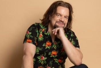 A smiling man seated cross legged.
