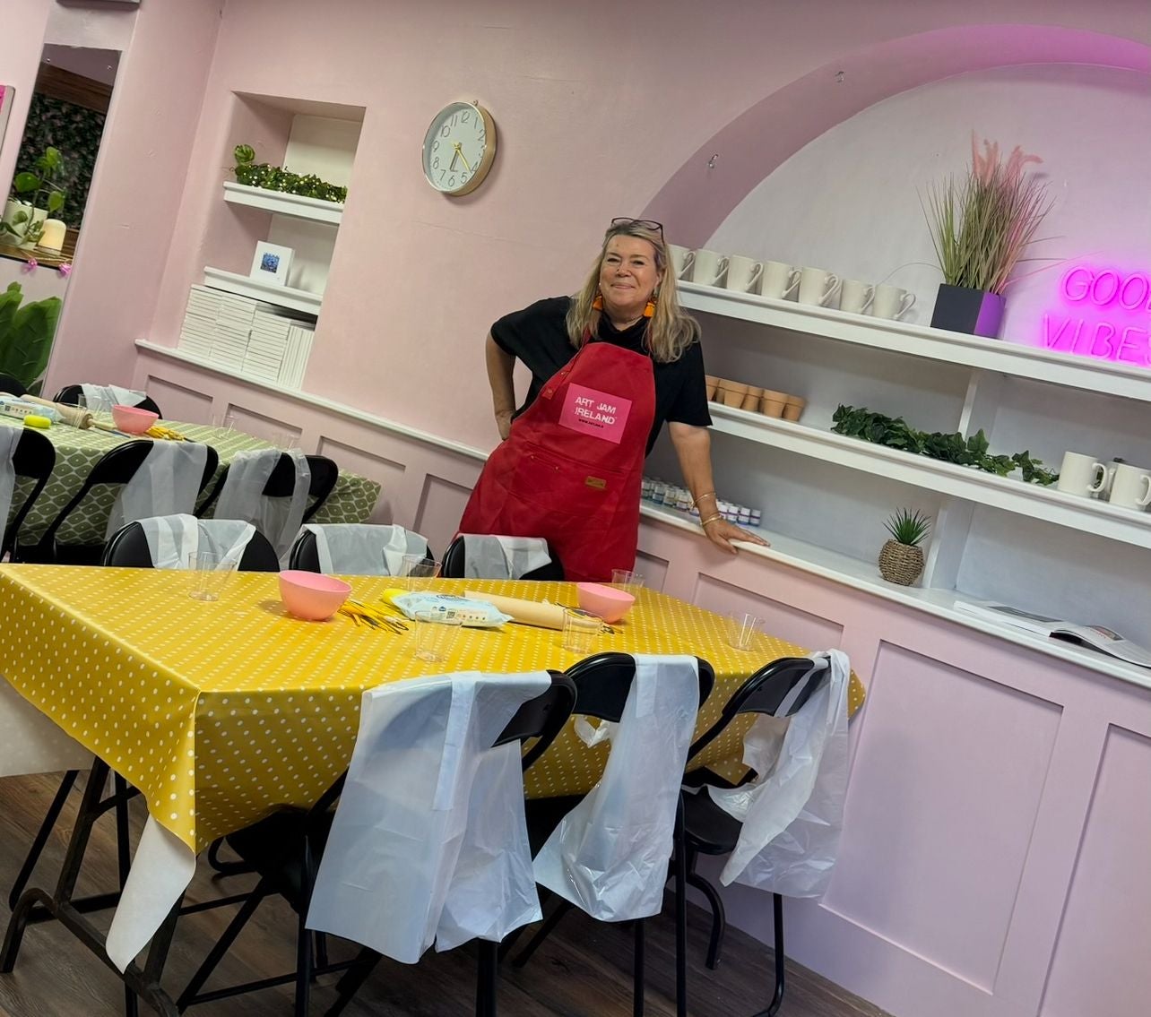 Person wearing a red apron standing by a table with a yellow tablecloth in a room with pink walls