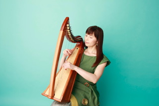 A seated woman playing a small wooden harp against plain green background.
