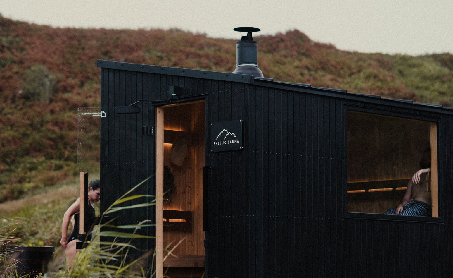 Two people using Skellig Sauna a lady entering the sauna and a gentleman relaxing inside