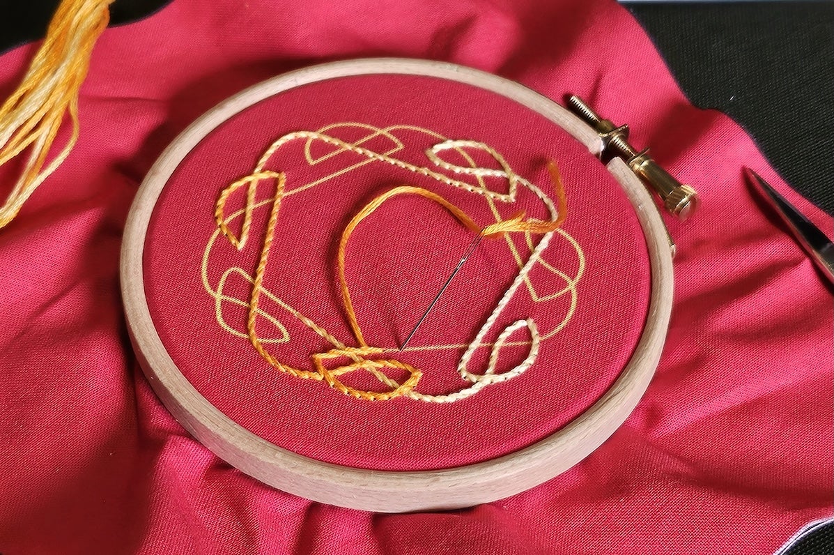 A large piece of red cloth with centre in a round wooden ring with yellow pattern embrioded on.