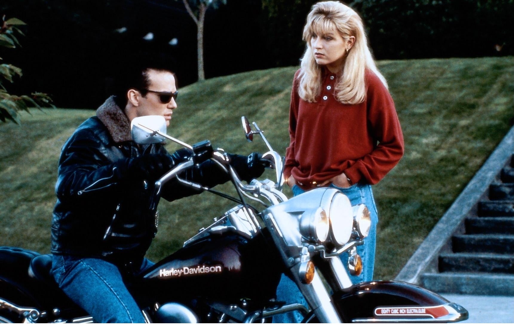 A young woman is speaking to a young man on a motorcycle.