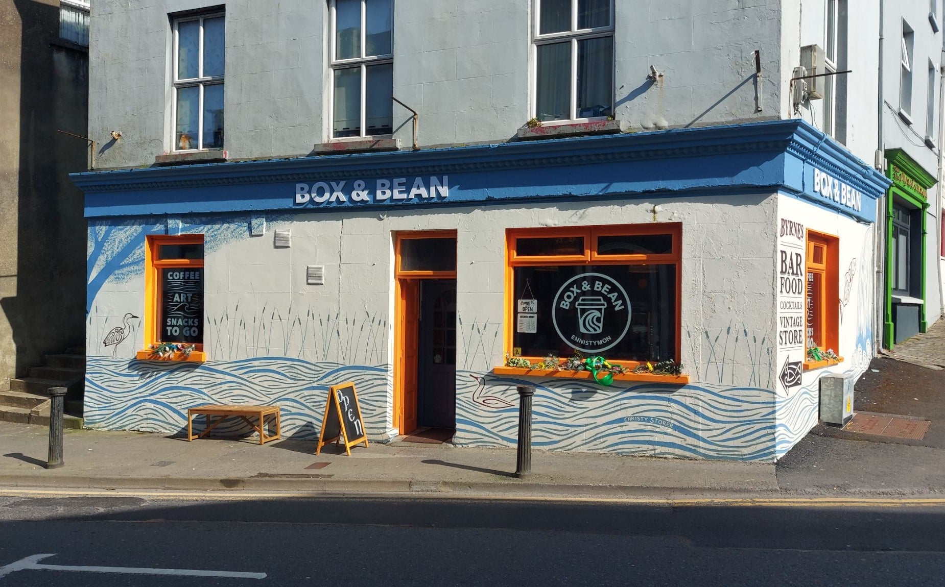A café with orange window and door frames and a bench and sandwich board outside