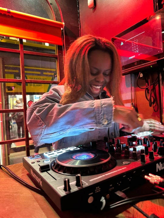 A laughing person standing at a small DJ mixing desk.