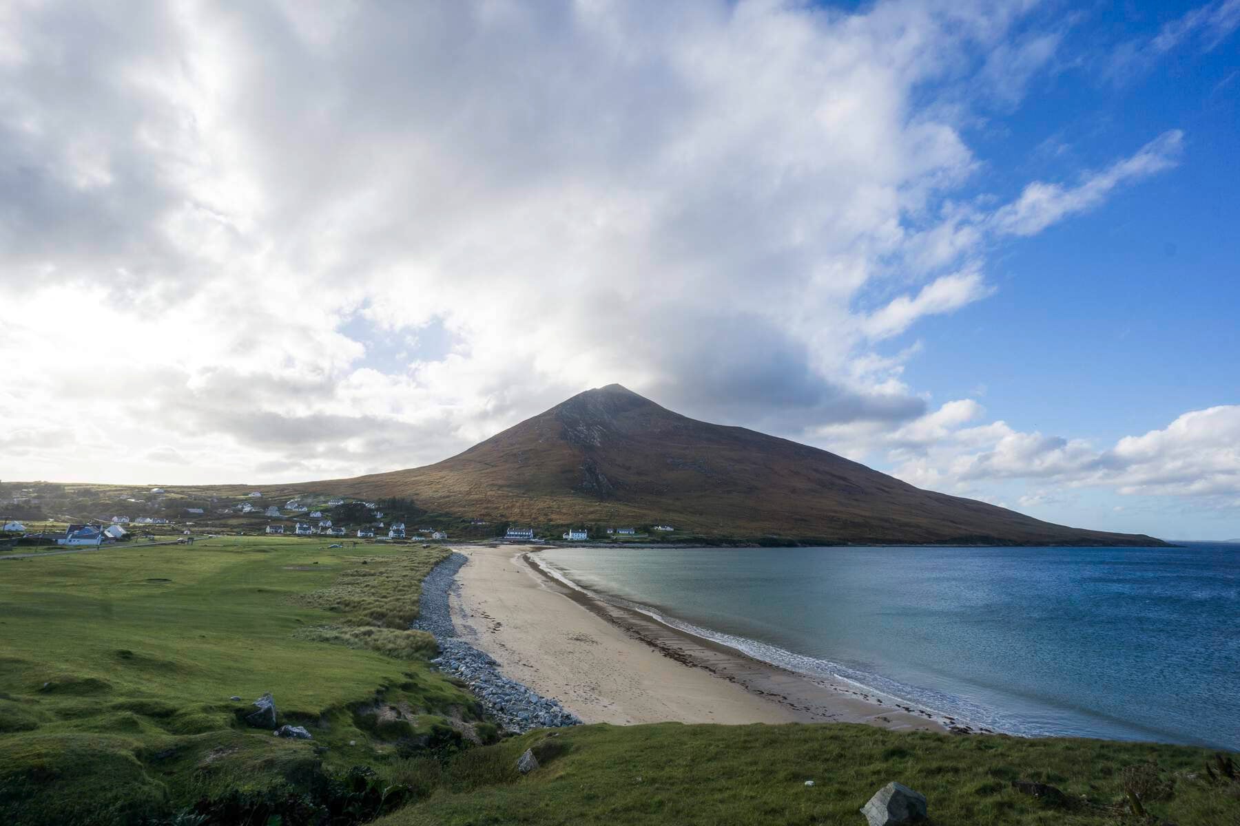 Beach in the forefront with a mountain at the end of the beach