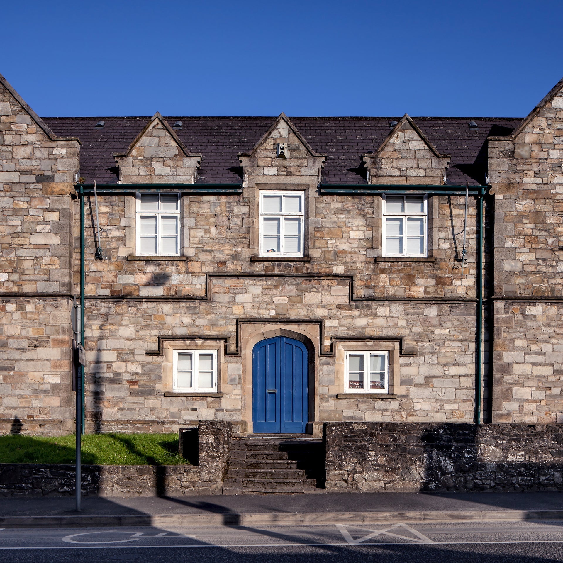 Stone building with five white windows and a blue door and steps in front