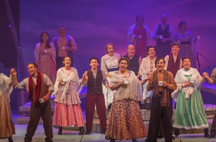 A large group of people in costumes singing on a stage