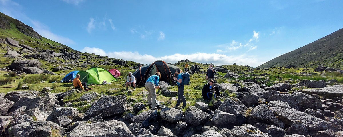 A group of climbers setting up camp up a mountain with coloured tents visible in the picture