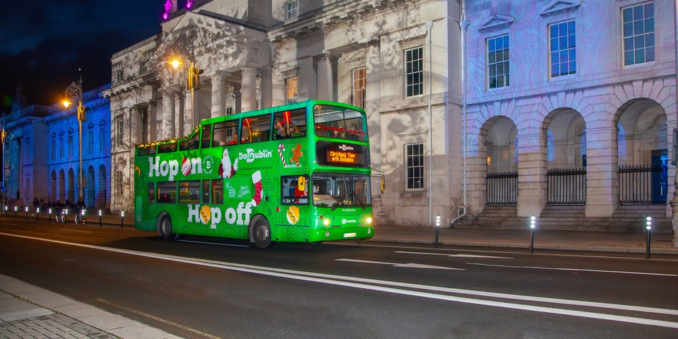 A green double decker bus at night outside old city buildings