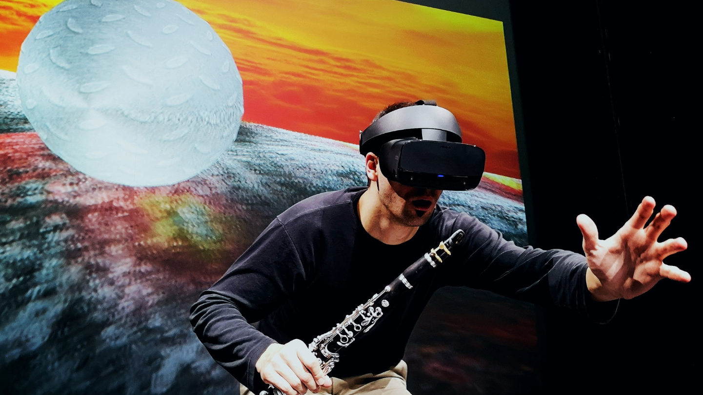Music Current 2026 _ Ressi Benes, a man wearing a VR headset and holding a clarinet is reaching out with his other hand.