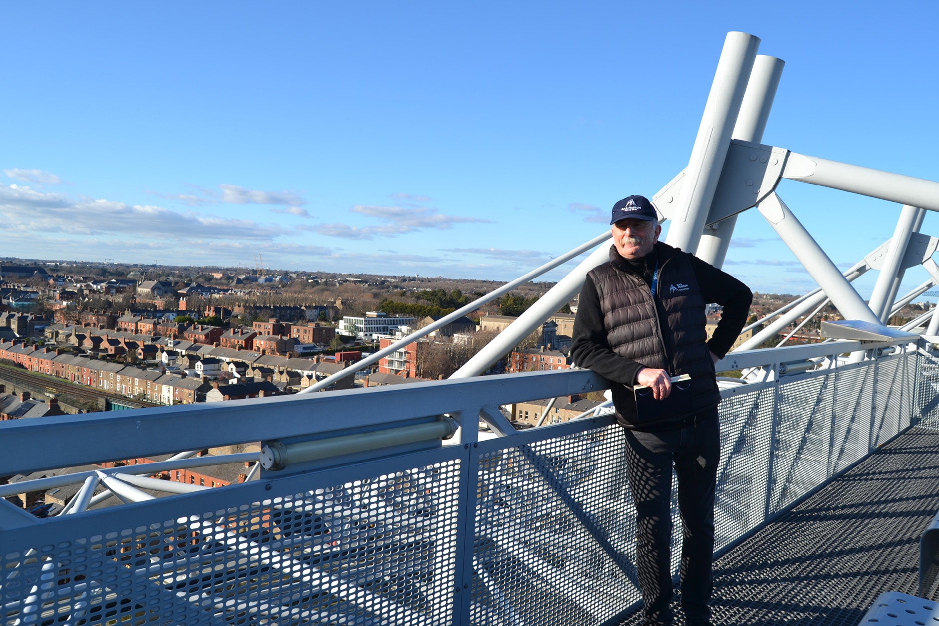 A man leaning on a rail overlooking a city on a sunny day.