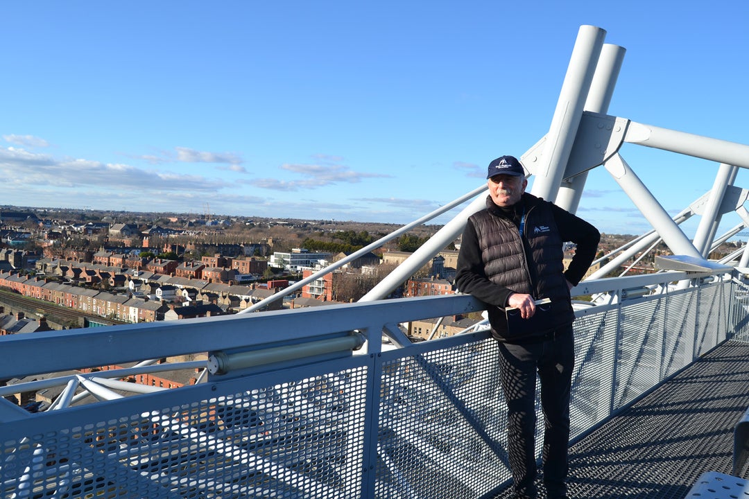 A man leaning on a rail overlooking a city on a sunny day.