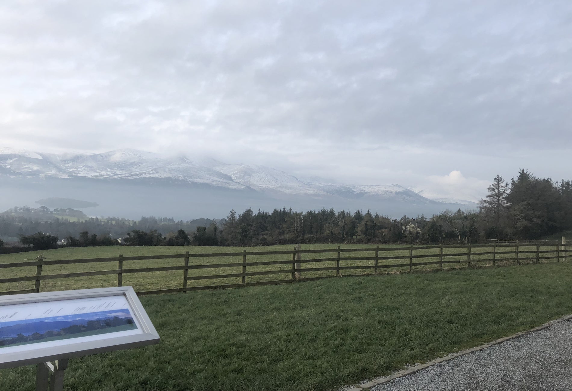 Wooden fence through a green field with snow capped mountains in the background 