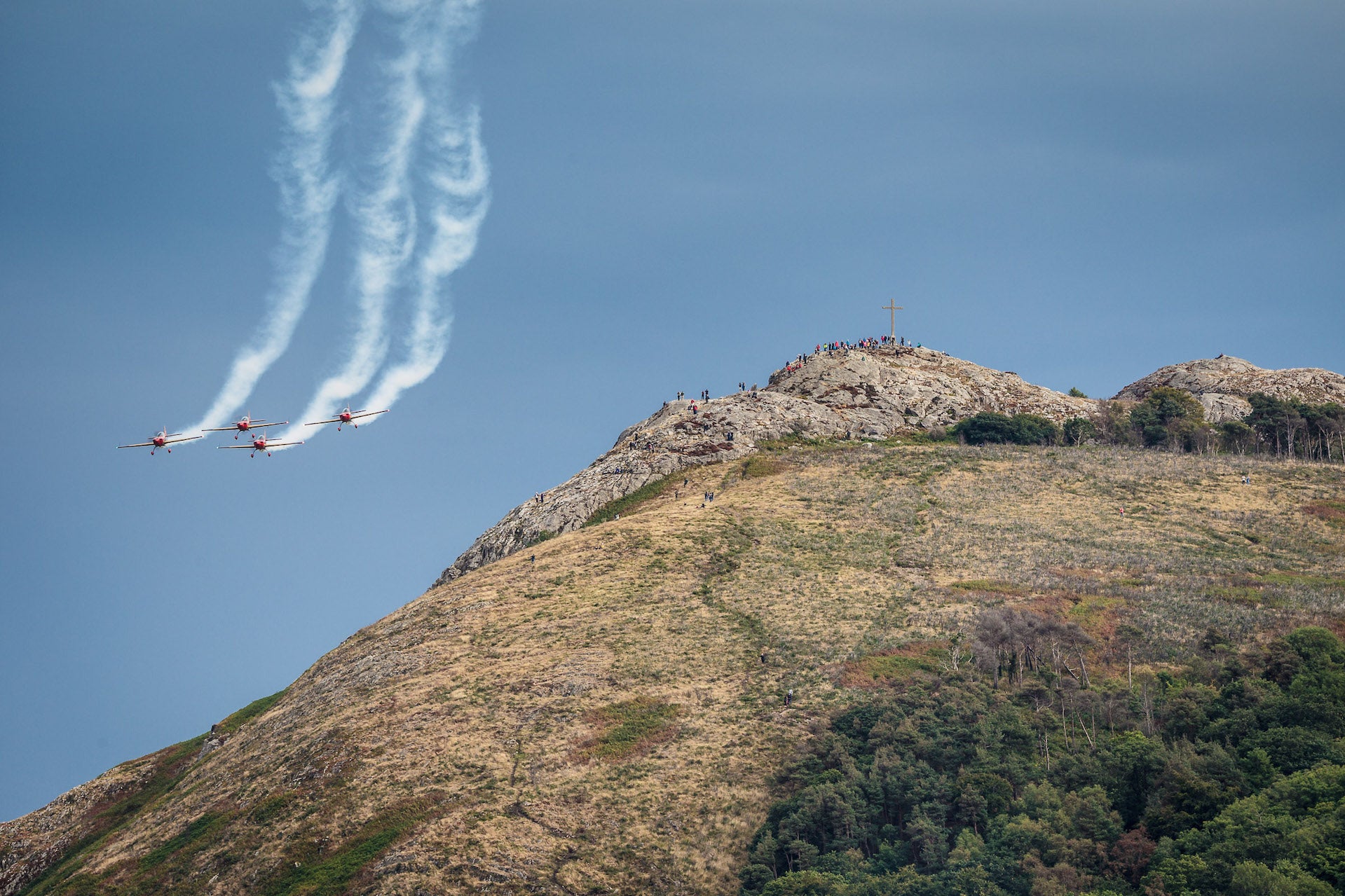 A large rocky hill with 4 jets with white plumes flying in formation to the left.