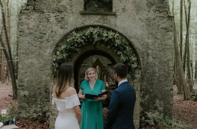 A bride and groom at a ruined archway standing in front of a celebrant