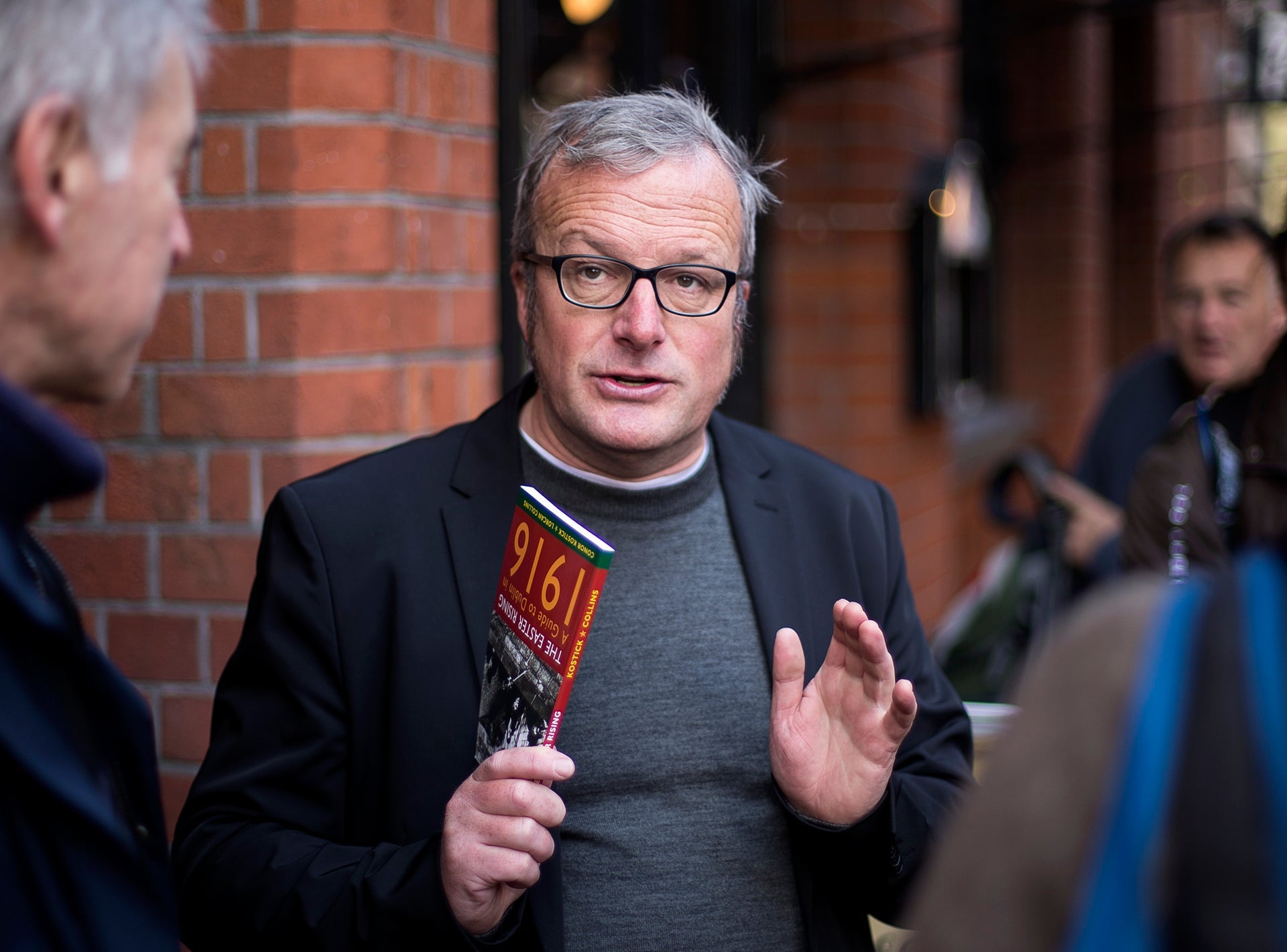 The tour guide holding a book about 1916 while speaking to the group