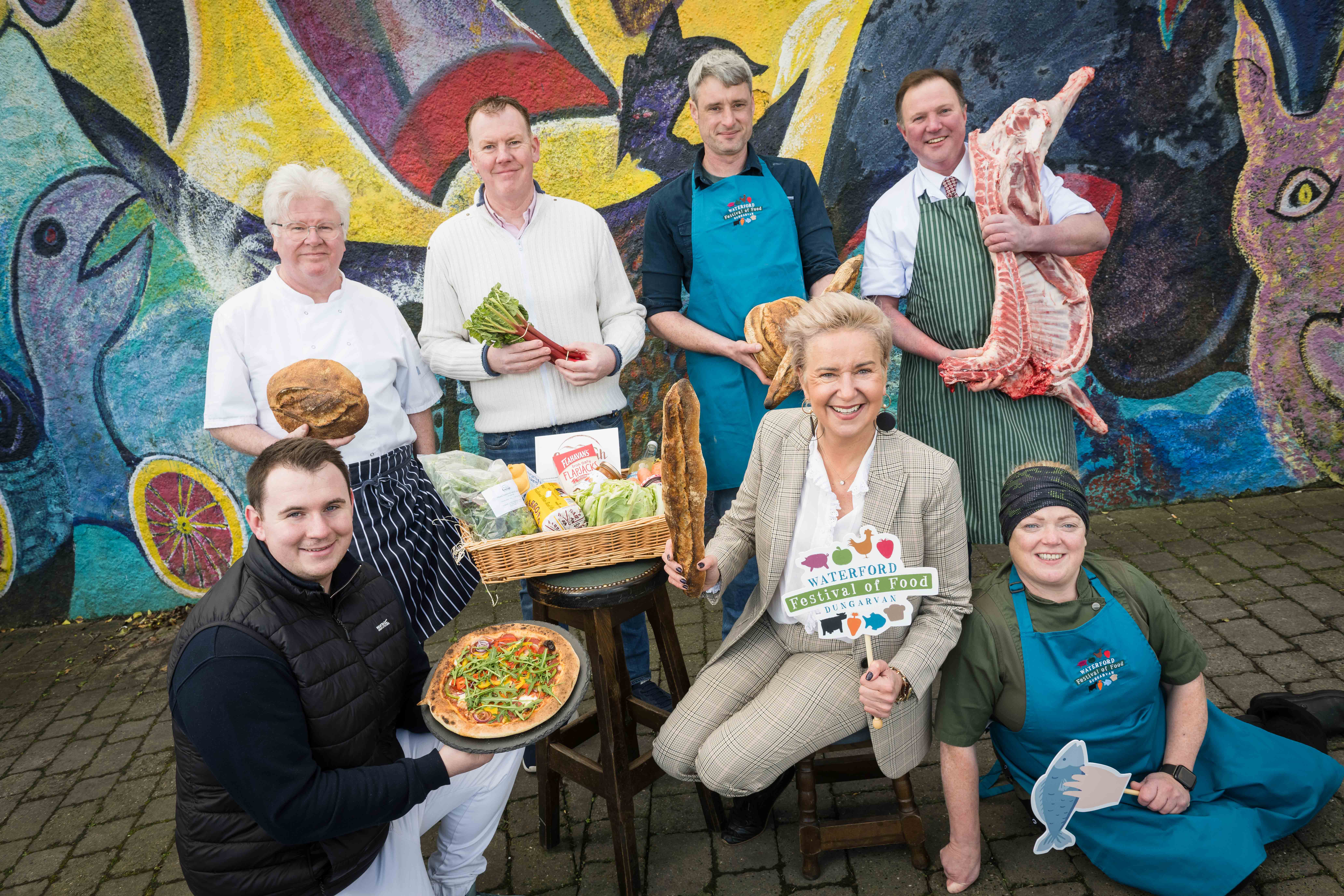 A group of smiling people each holding either food produce or small hashtag signs