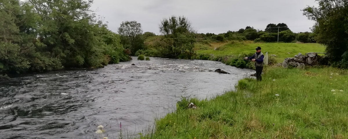 A lone fisherman standing on a river bank with fishing rod in hand