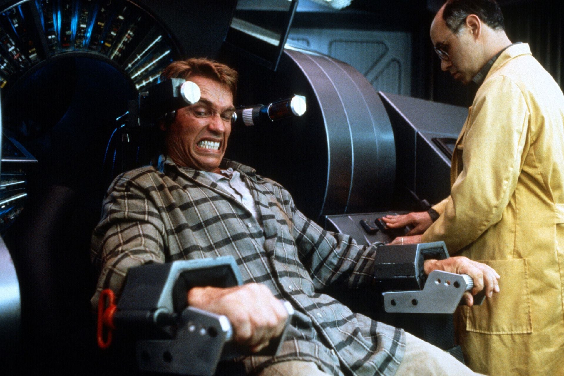 Arnold Schwarzenegger is strapped to a machine while a scientist operates it.