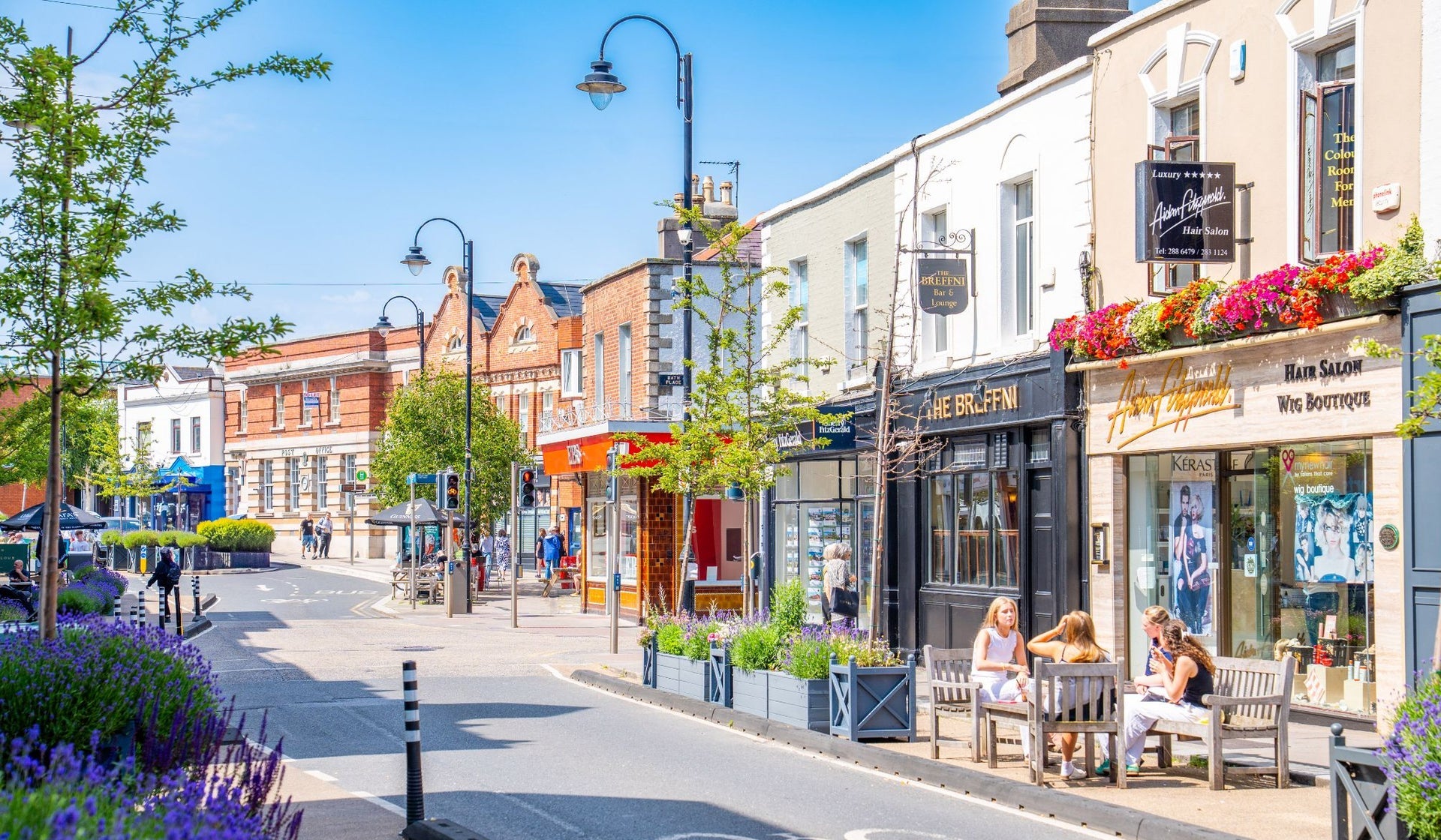 Colourful shopfronts on a Blackrock Village street with trees and planters