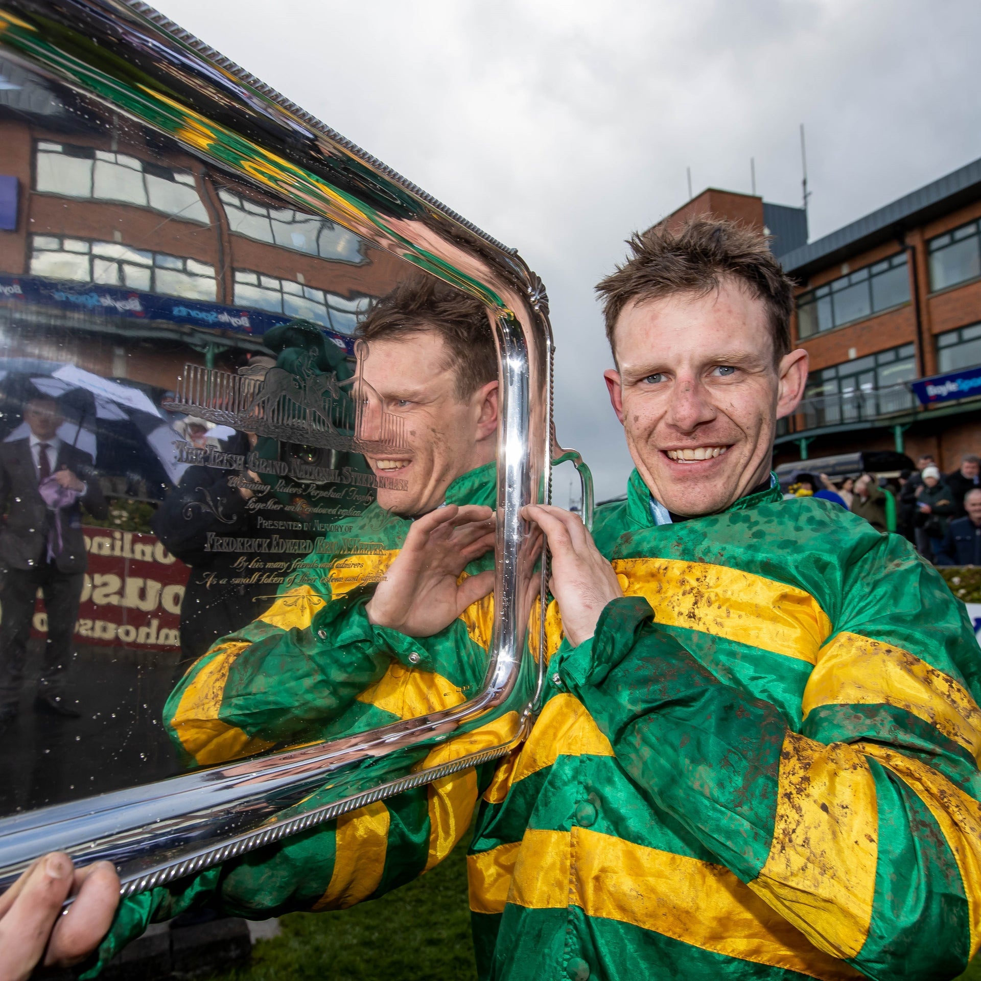 Jockey in a green and gold top holding a silver tray shaped award