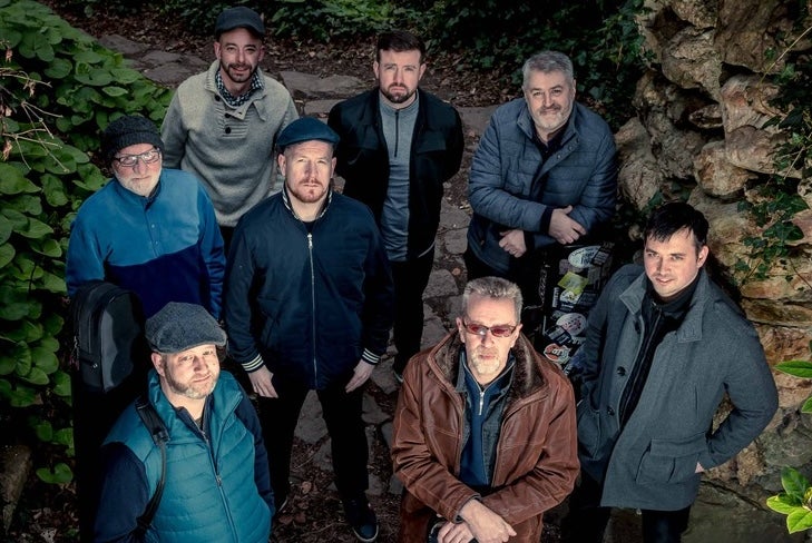A group of 8 men in outdoors clothing looking upwards at camera
