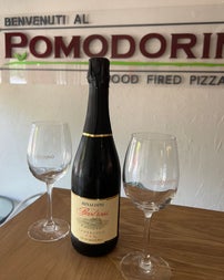 An Italian bottle of champagne with two glasses on a table with a restaurant name on the wall behind them
