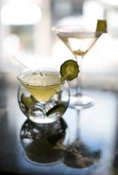 Two cocktail glasses with a clear liquid garnished with a slice of cucumber