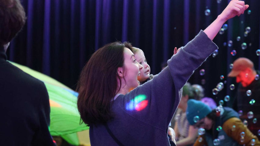 A laughing woman holding a baby pointing upwards with bubbles in the background.