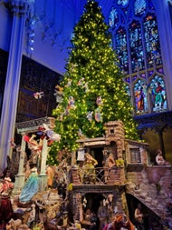 An elaborate, hand-crafted nativity scene sits beneath a glittering Christmas tree inside the Gothic Chapel Royal, its stained-glass windows glowing blue—a hidden gem showcasing Christmas tradition amid stunning ecclesiastical architecture.