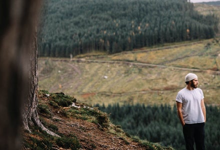 James Vincent McMorrow live. A man with hands in pockets is standing outdoors under a large tree with distant hill with trees.