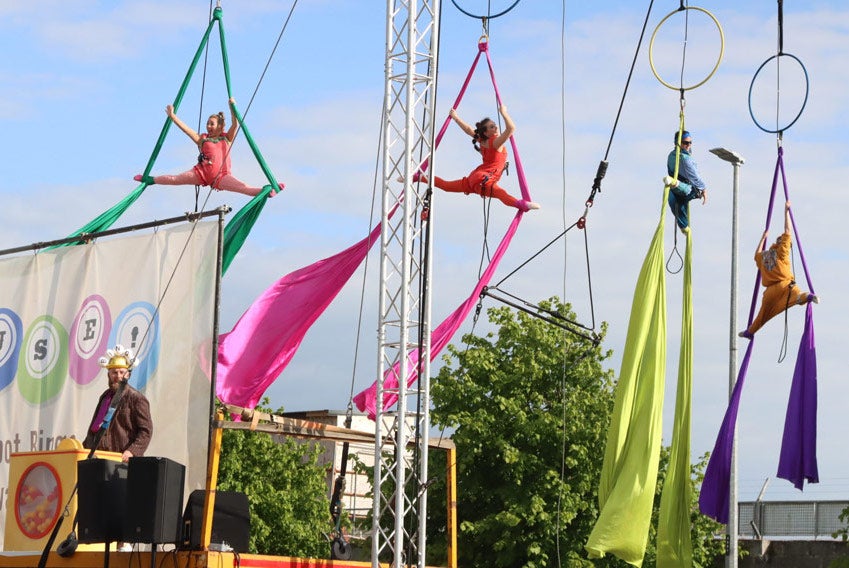 In the air, hanging from hoops attached to ropes, 4 performers with different coloured materials