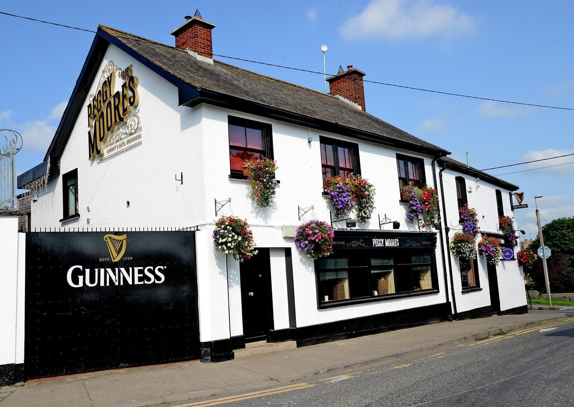 Exterior of a black and white pub on a street with flowers by the windows and in hanging baskets