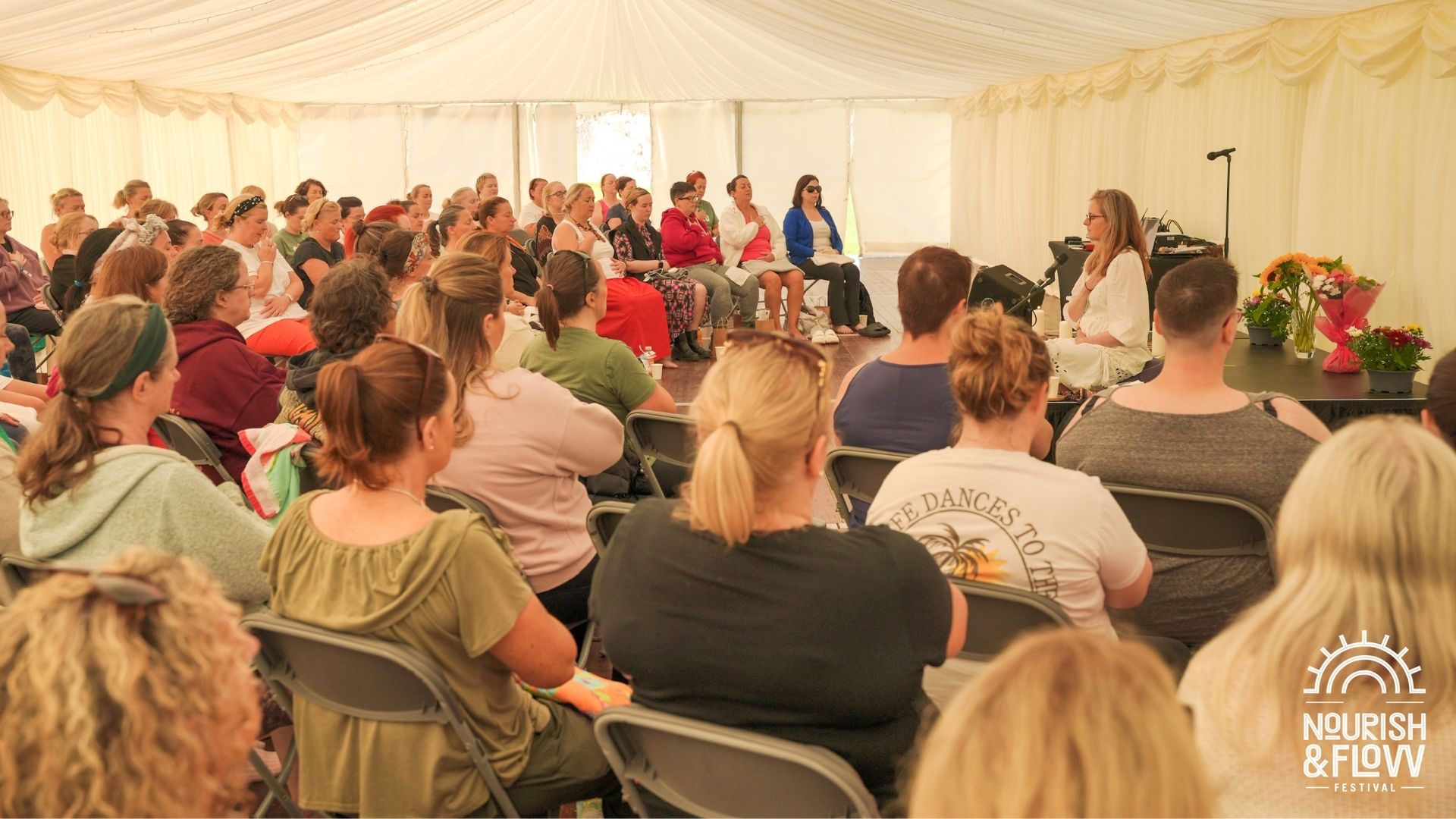 An audience in a large tent listening to a person at the front talking.