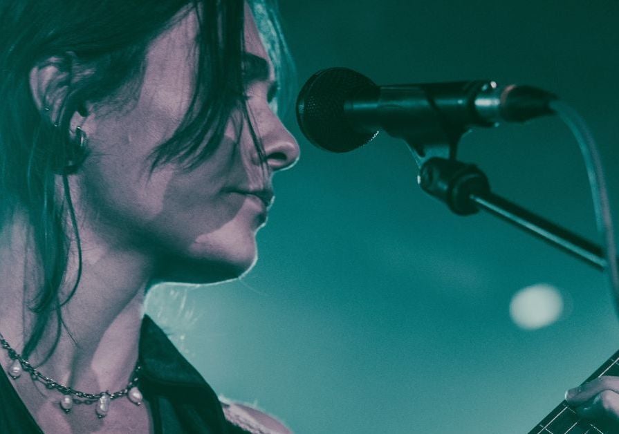 Close up side view of woman in front of a mic on a stand, playing a guitar.