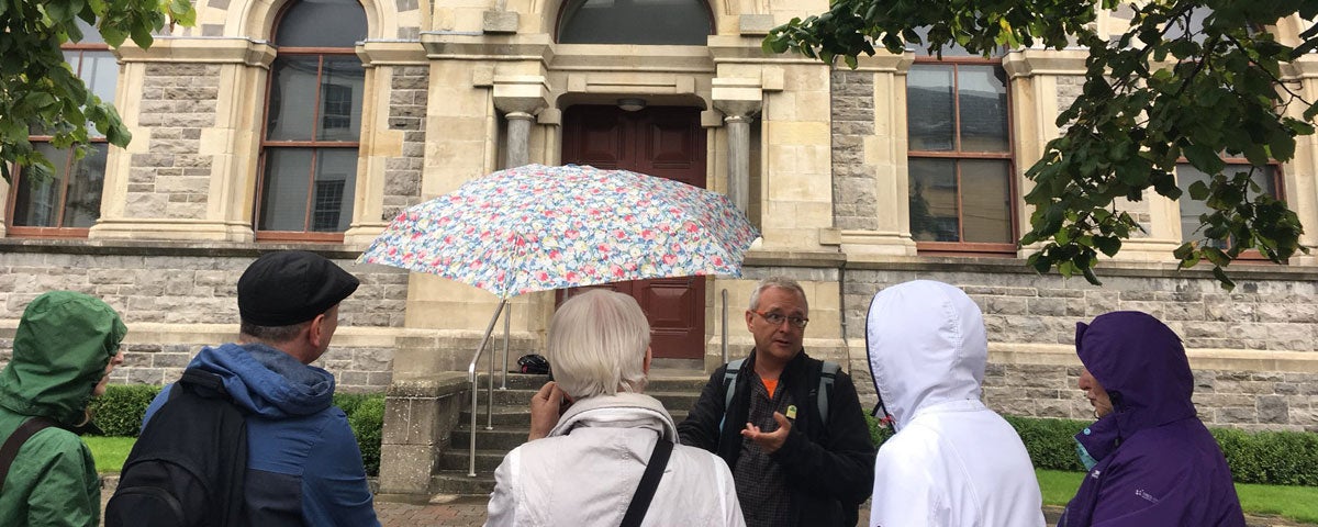 A group of people standing outside an old building while a tour guide speaks to them