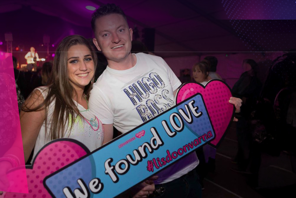 2 smiling people holding pink, large hearts and a hashtag sign.