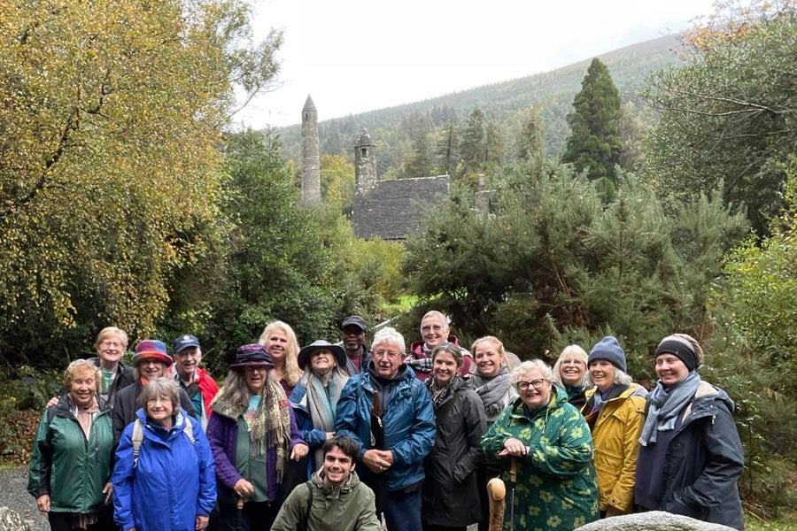 A group on a Glendalough Musical Tour with the round tower and Saint Kevins church in the background