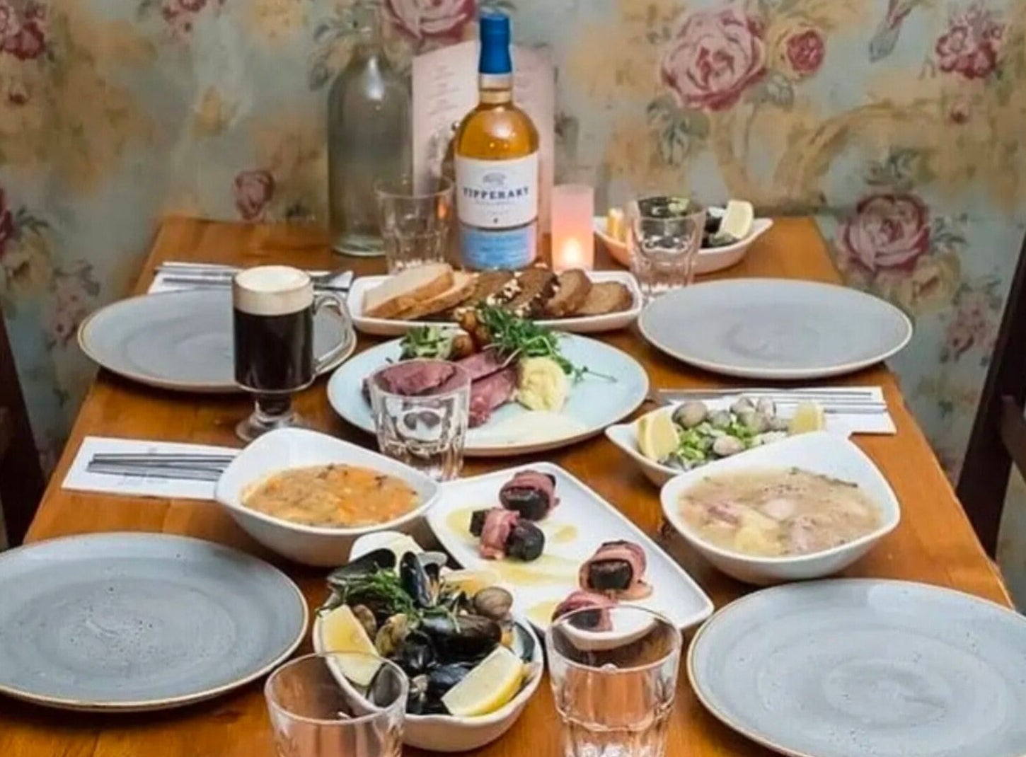 Table with four grey plates an assortment of food dishes glasses a bottle of wine and a candle