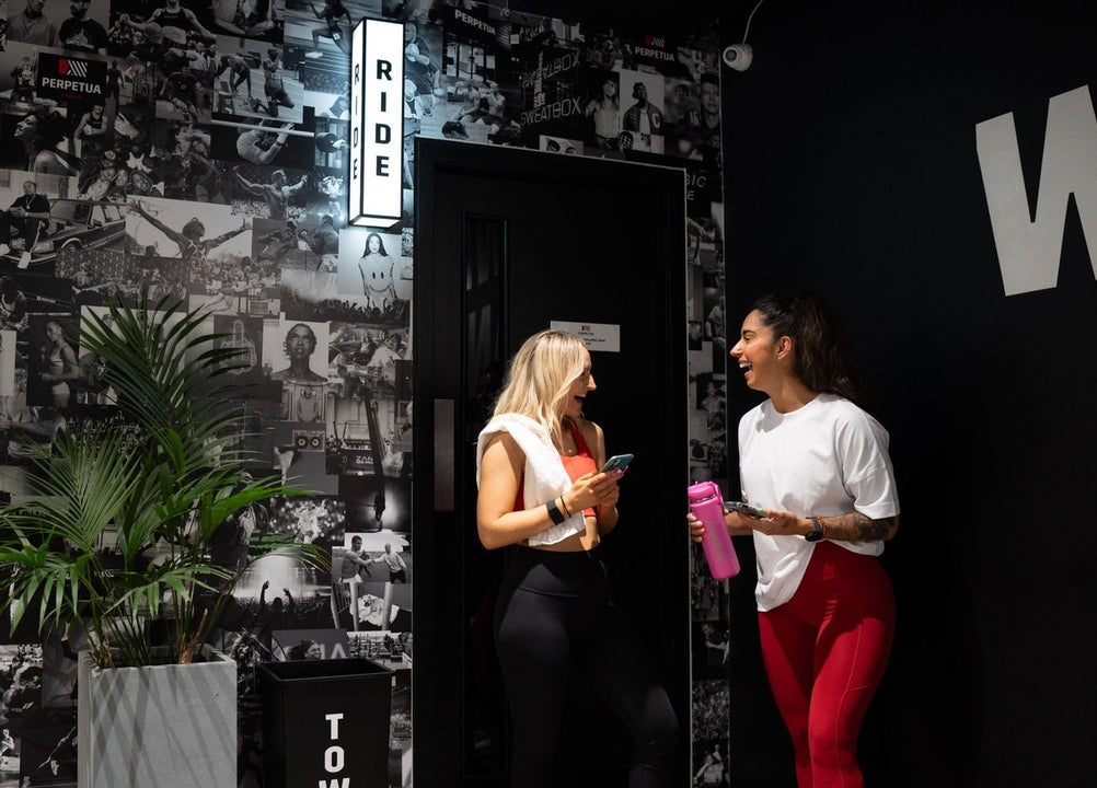 Gym members chatting against a dark wall of fitness imagery