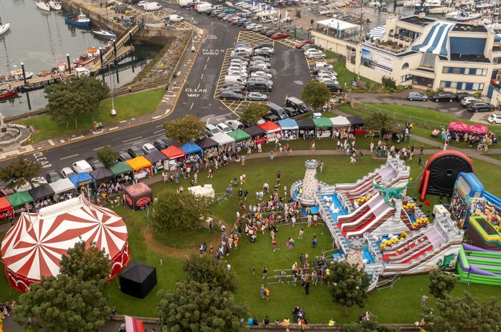 Howth Maritime & Seafood Festival 2026 - viewed from above, a grassy area containing a big top tent, large bouncy slides, rows of stalls in a town setting