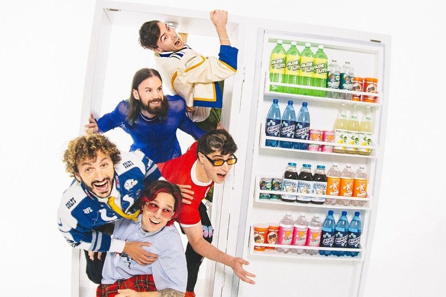 5 men bursting out of a large fridge full of bottles in the door