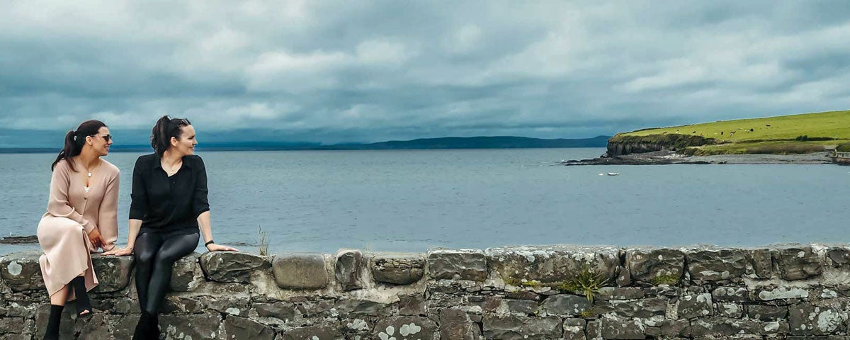 An image of the two owners sitting on a wall overlooking the harbour