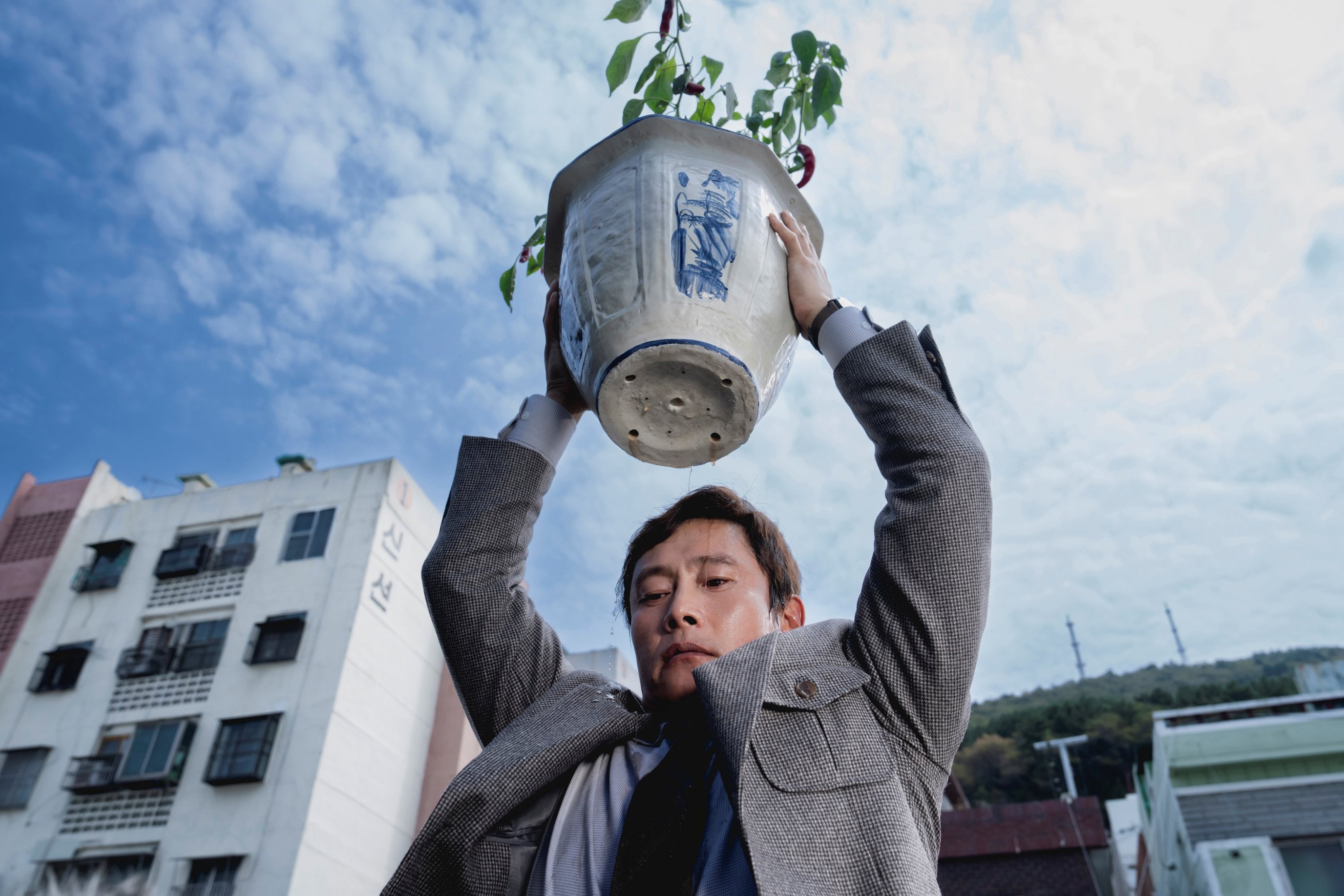 A man is holding a large potted plant over his head, as if to throw it.