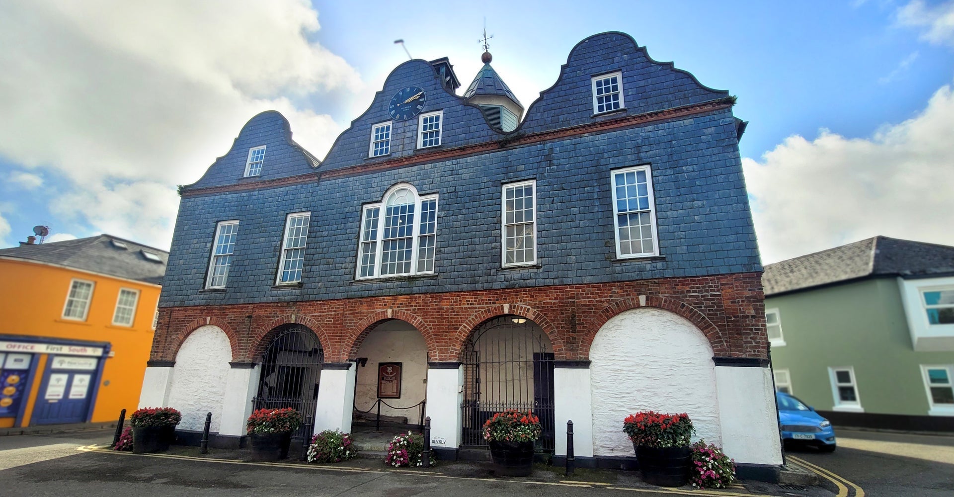 Slate red brick and white exterior of a dutch style building with three open archways and flowers outside