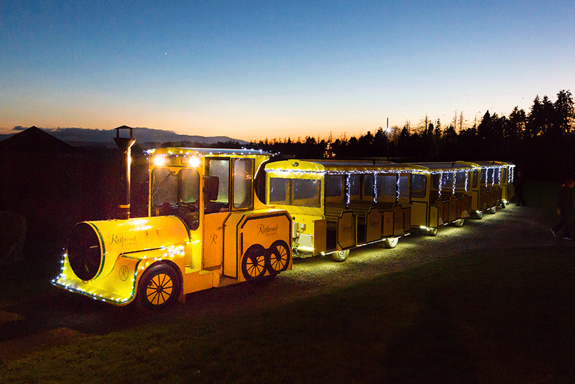 A small yellow train with carriages lit up at dusk