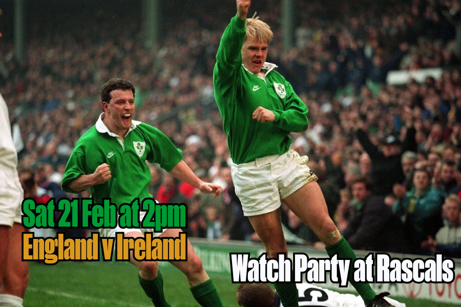 2 men playing rugby in green shirts with large crowd in background.