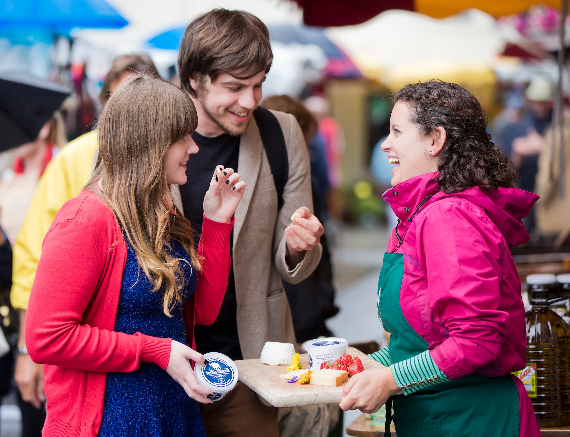 A merchant offering two people samples at the Galway Farmers' Market.