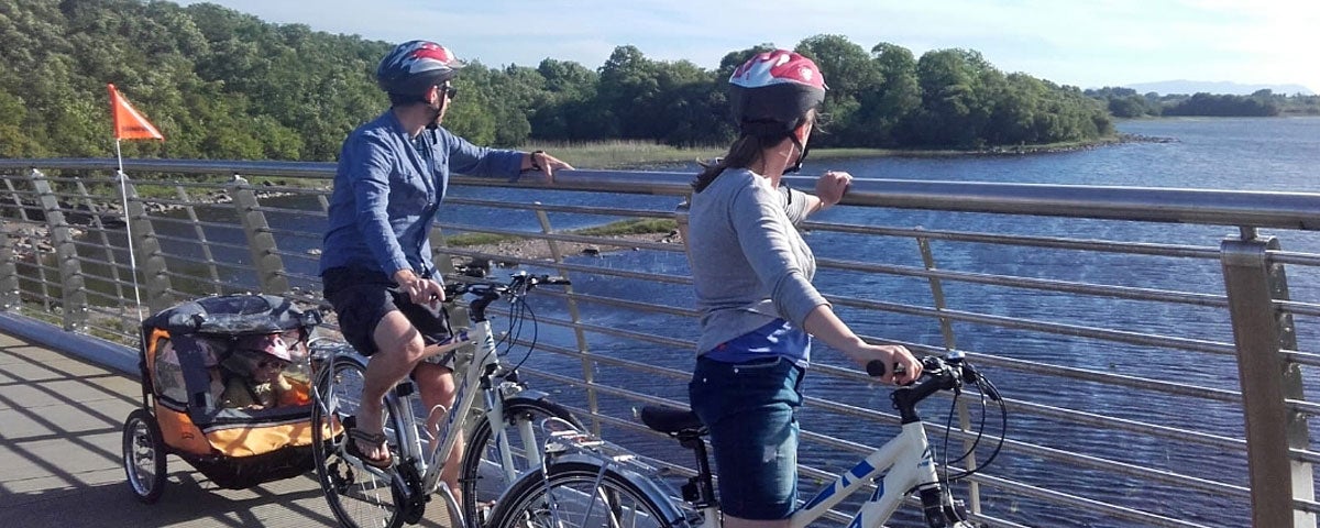 Bikes & Boards family on bikes viewing a river from a bridge