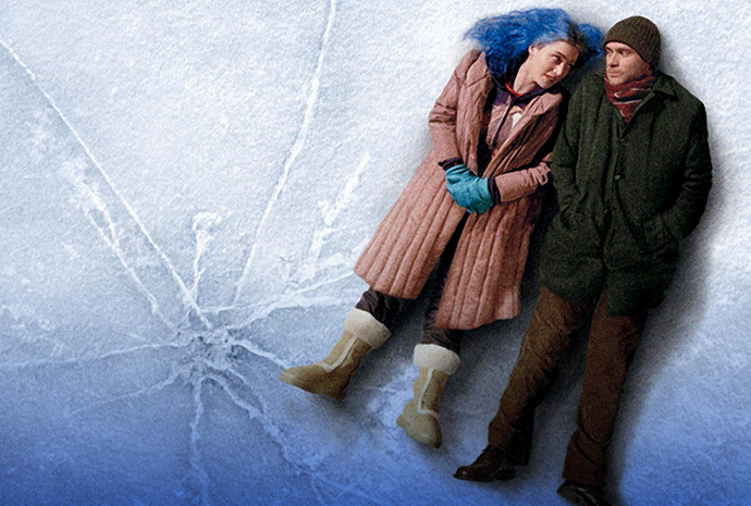 2 people dressed in winter coats are lying on their backs close together on icy surface.